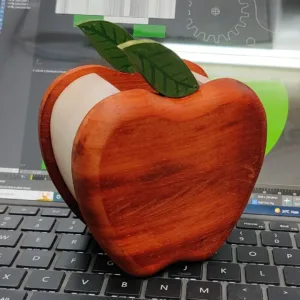 A wooden apple pen holder sitting on a laptop keyboard.