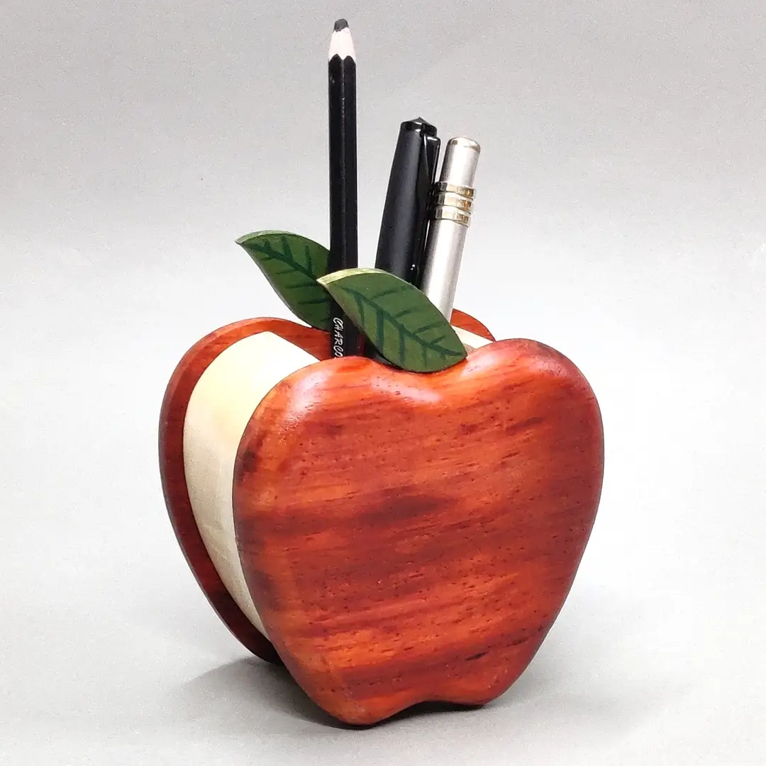 Apple Pen Stand A wooden apple holder filled with pens and a charcoal pencil.